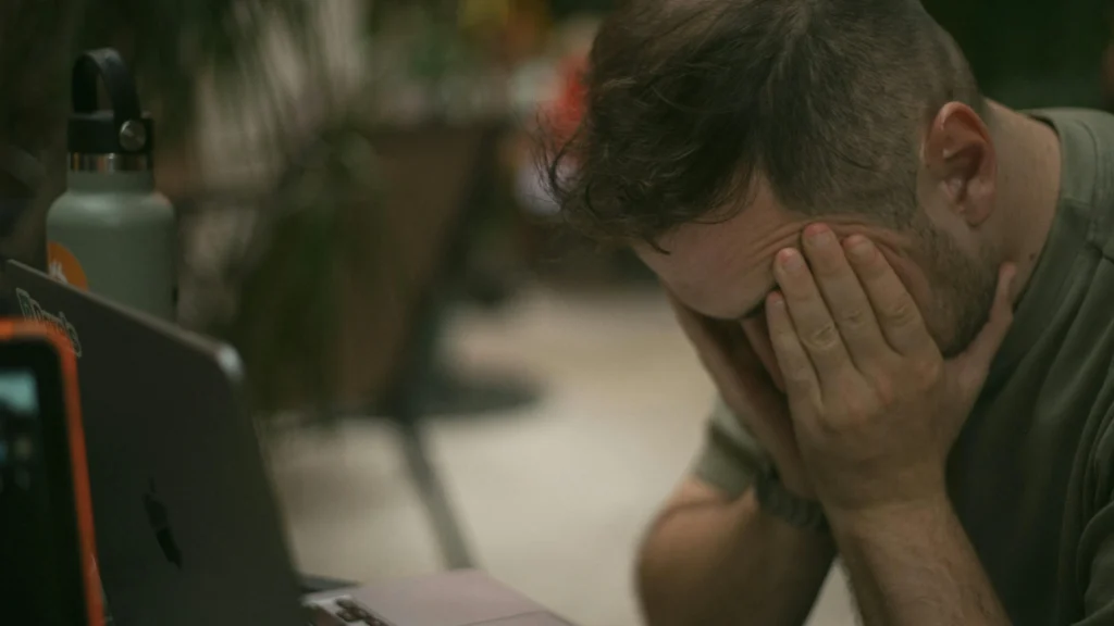 A person showing signs of stress while working on a laptop.